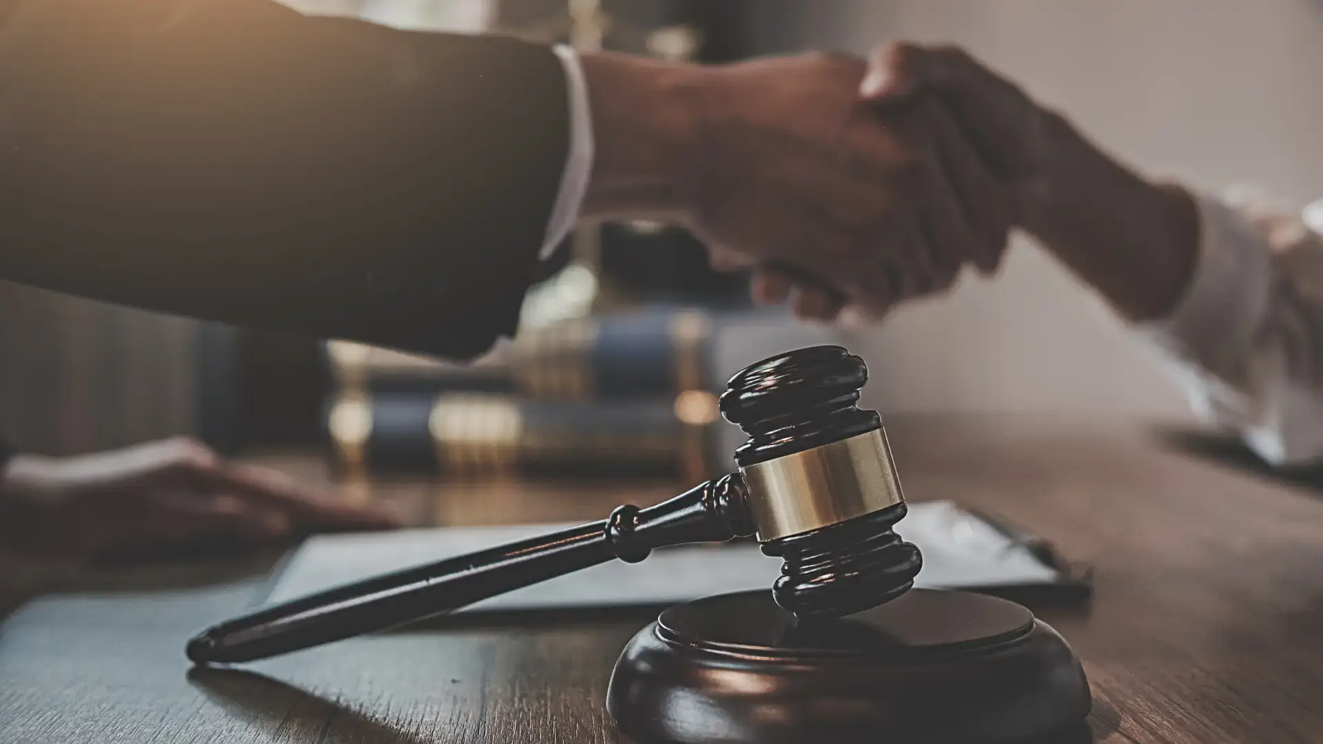 Gavel on a desk with a handshake in the background.